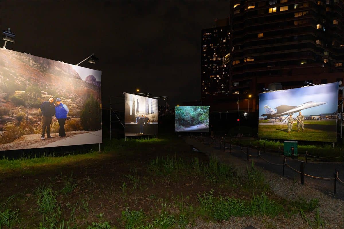 Outdoor view of the “Path of Liberty” exhibition at night, showcasing large illuminated portraits and landscapes against the Manhattan skyline.